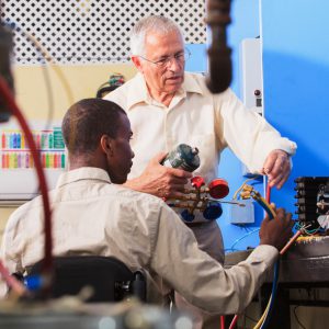 Instructor demonstrating air conditioner repair to a wheelchair user.